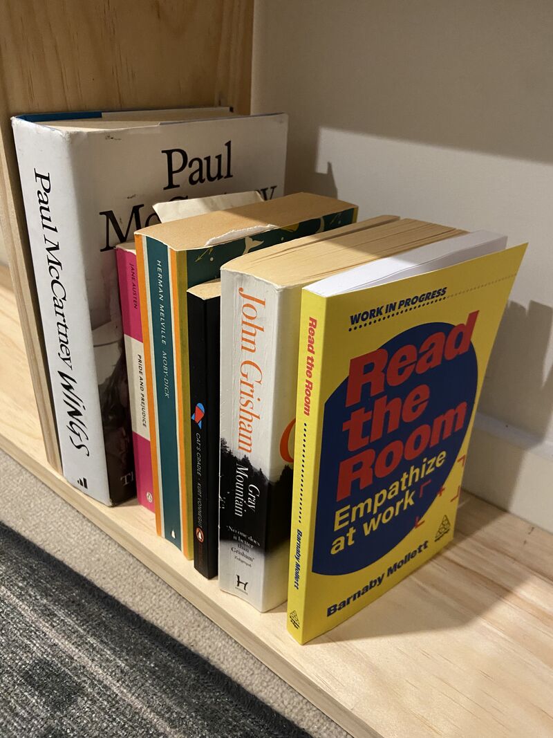 Stack of colorful books on a wooden shelf, including “Read the Room” ... and “Paul McCartney Wings.”